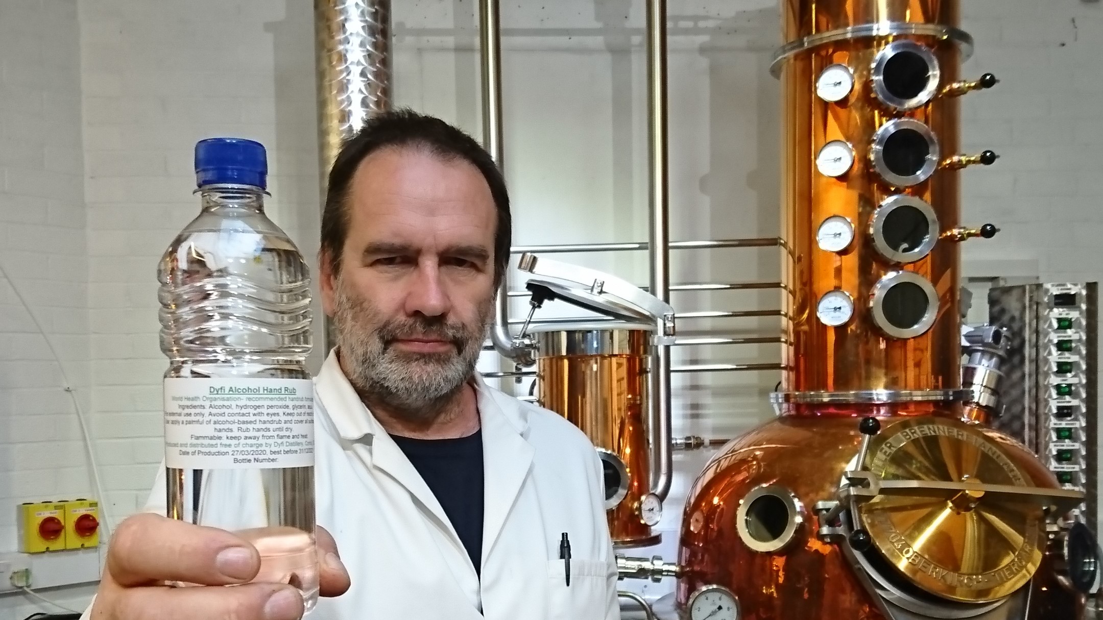 Man holding bottle of alcohol in front of distillery