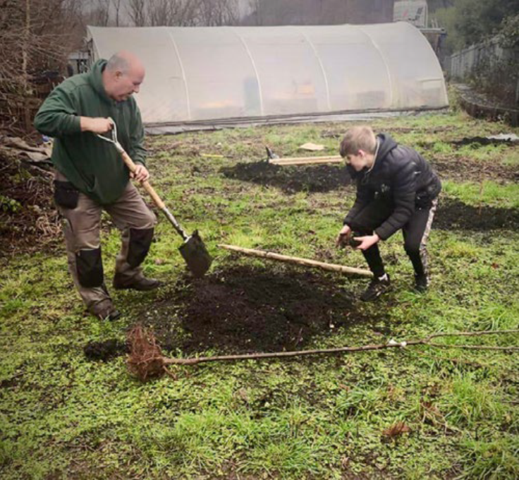 Two males in a garden, digging a hole.