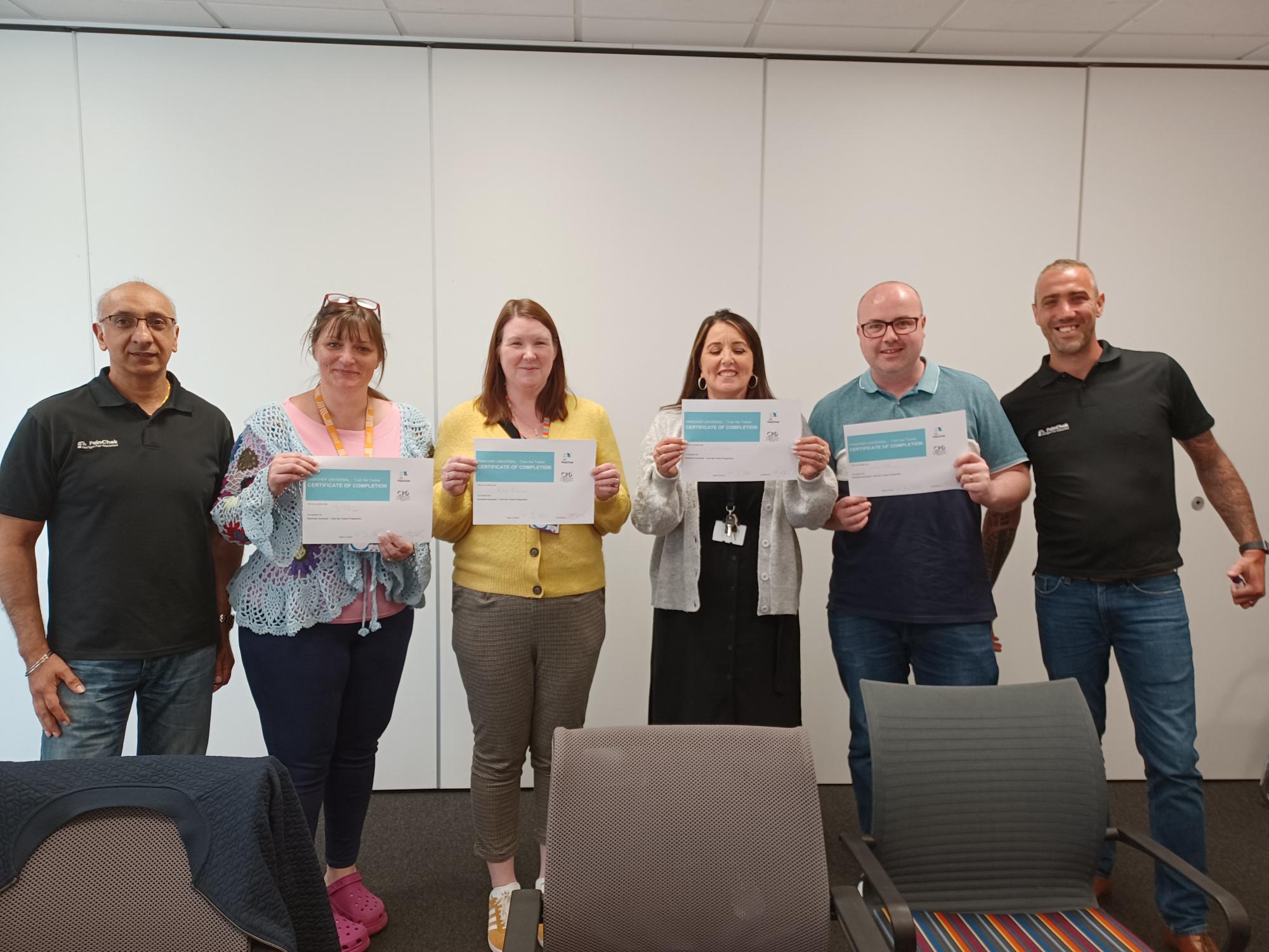 Six people stand smiling. Four people are holding certificates.