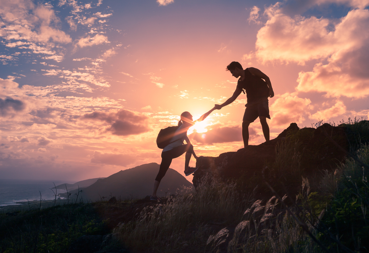 Two people climbing a hill in front of a setting sun