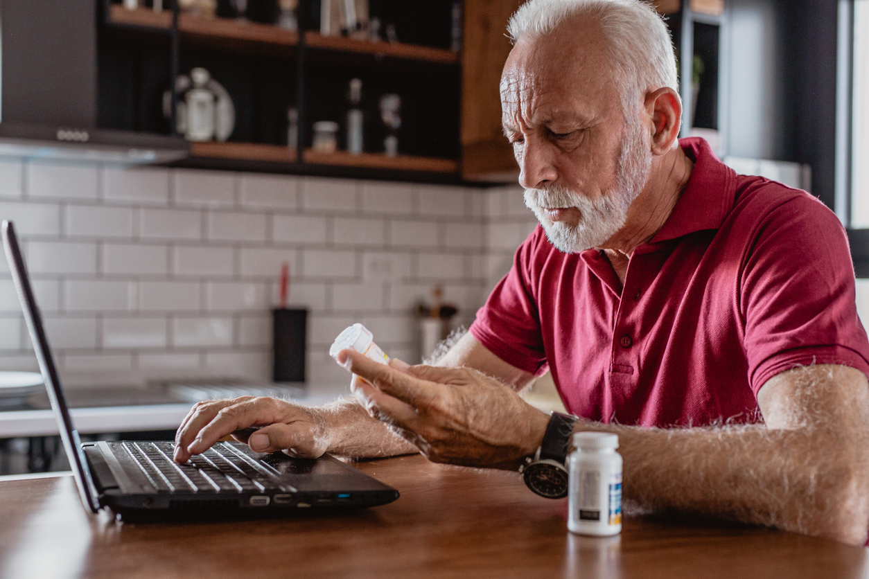 Senior man is looking for information about the medicine over the Internet. He is holding a medicine in one hand and he looks worried