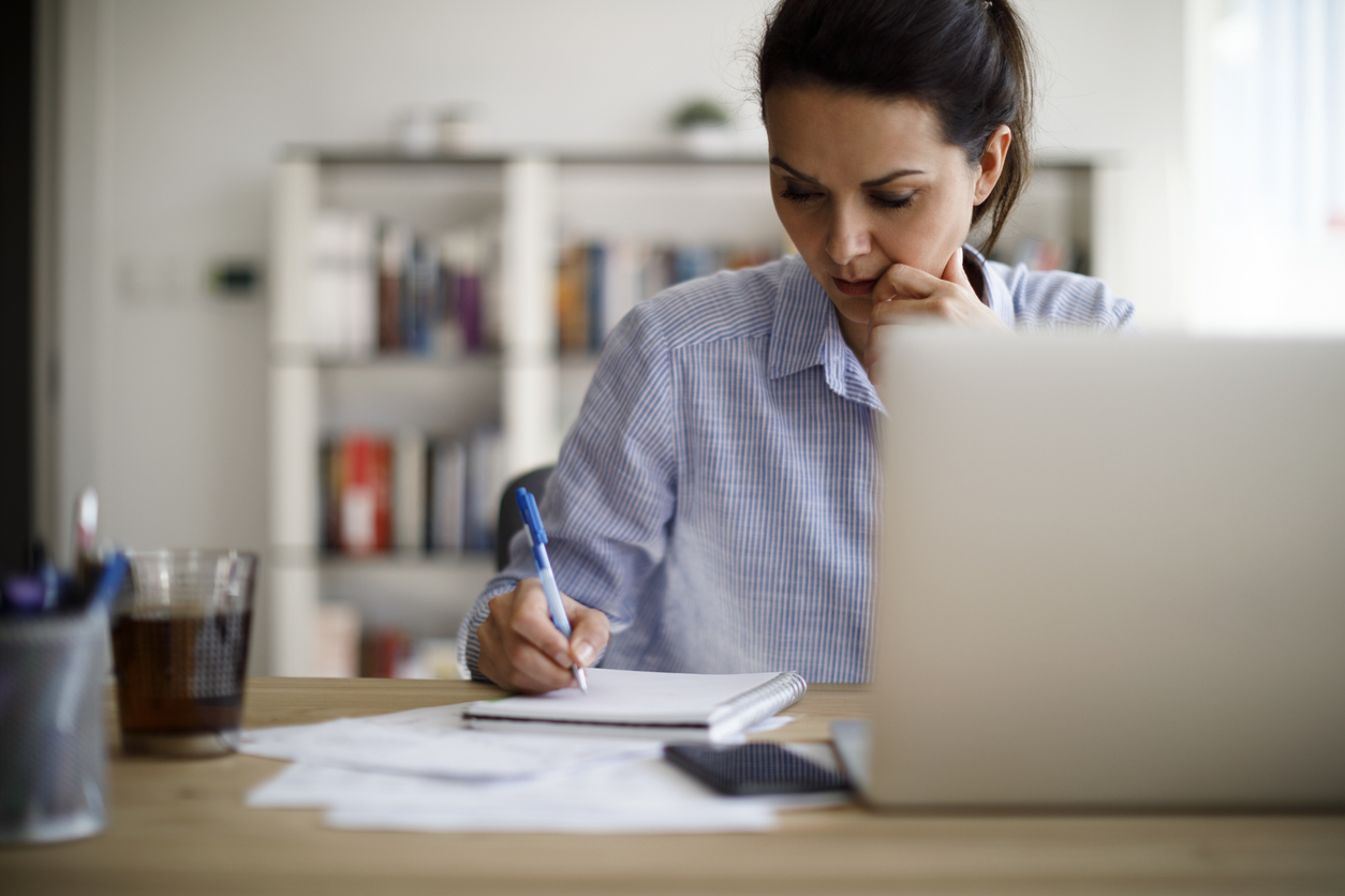 A woman writing notes during a virtual event, a silver laptop is in front of her