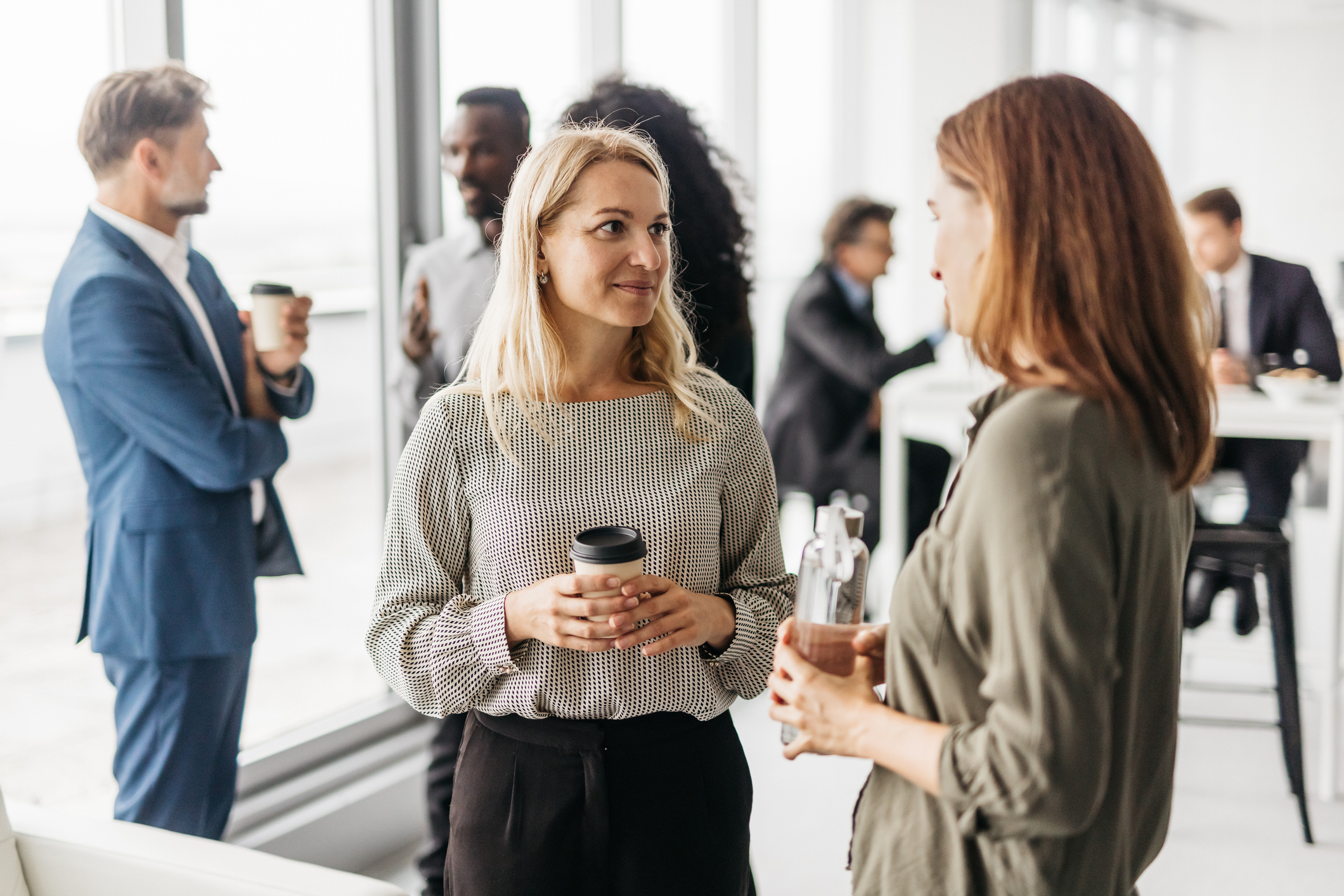 Two women talking at a conference, they are both holding coffee cups