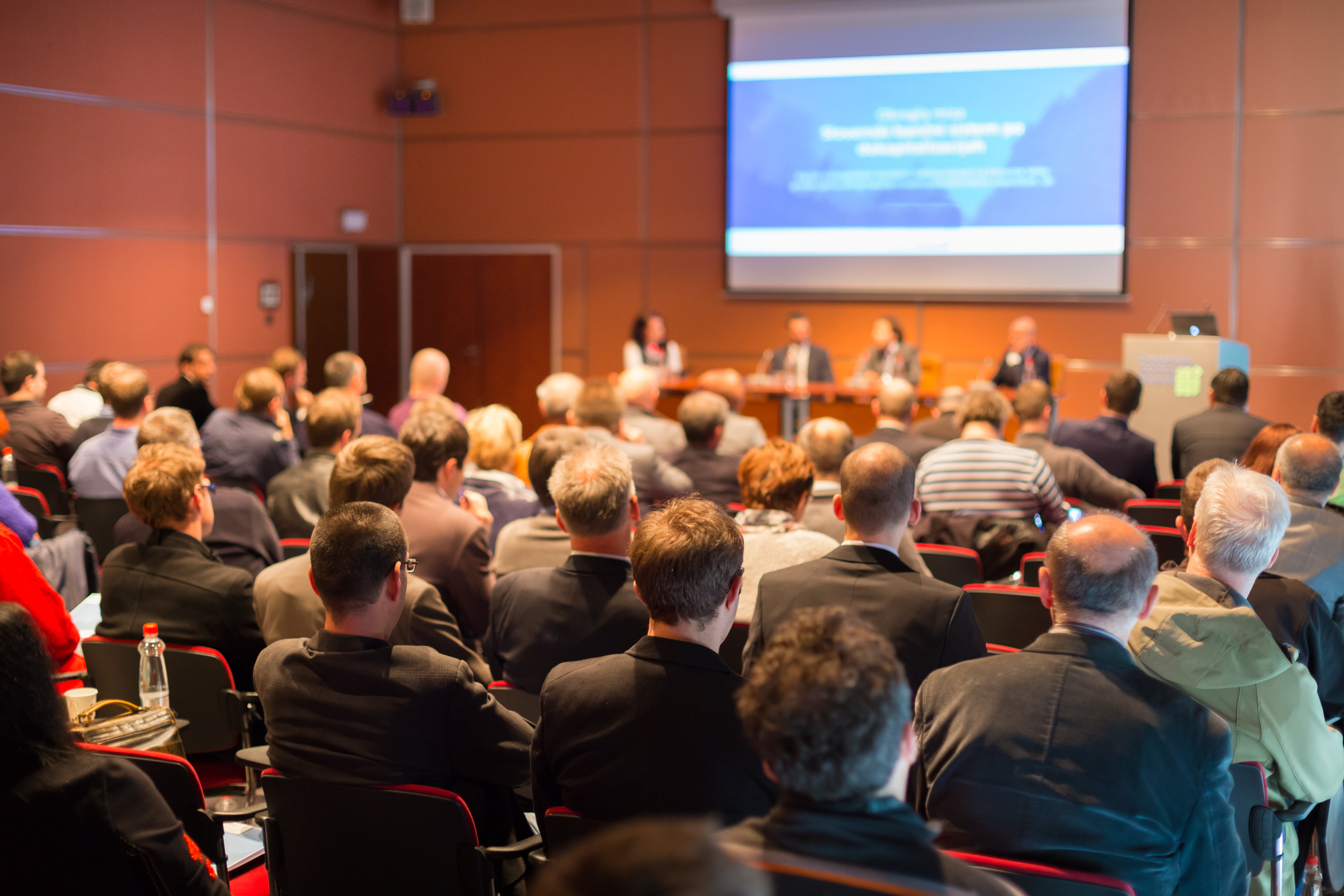 A large group of people at a conference, listening to a panel discussion