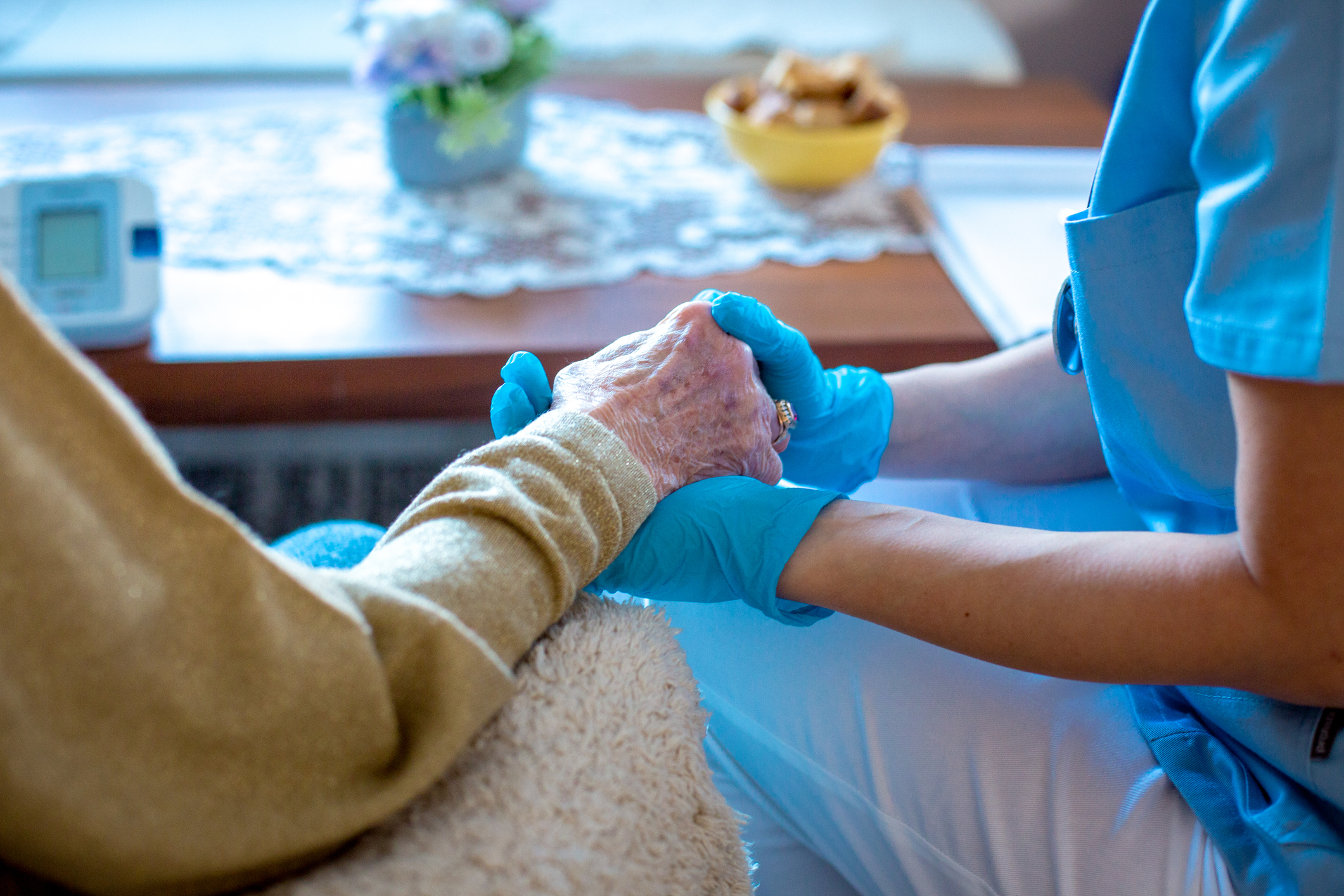 A care worker in blue gloves holding hands with an elderly person.