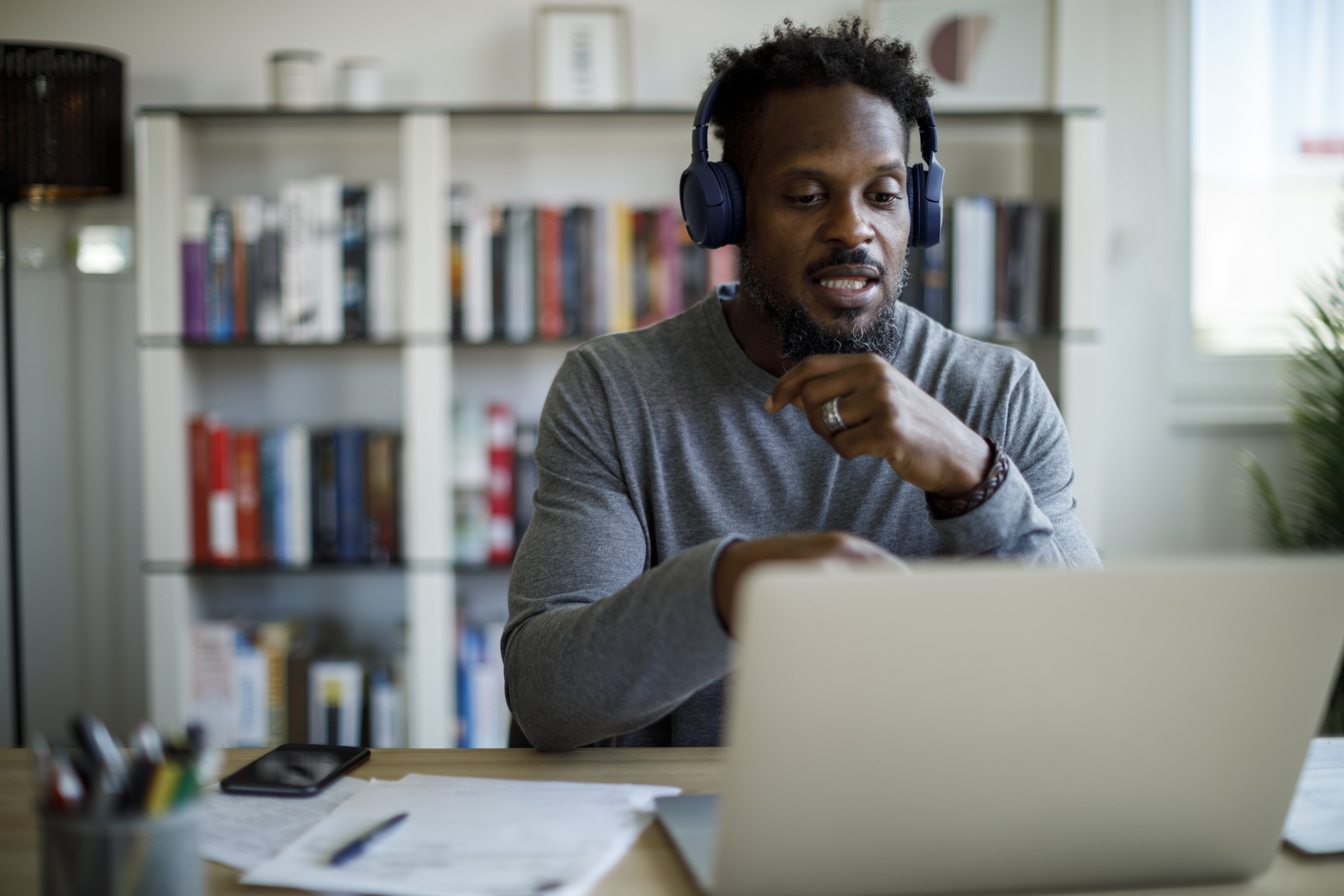 A man in a grey jumper looking at a laptop, he is wearing headphones