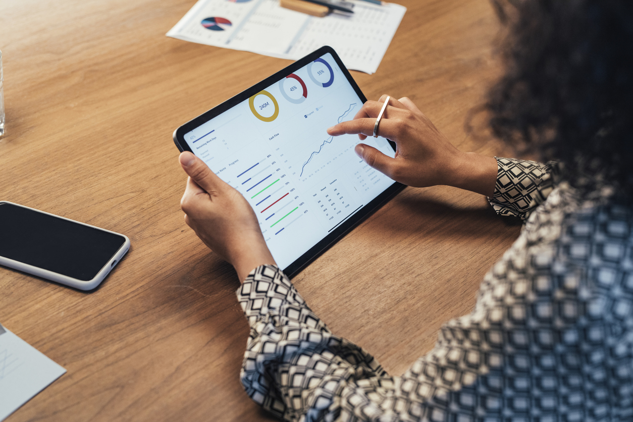 A woman holding an iPad, the screen shows generic graphs and data