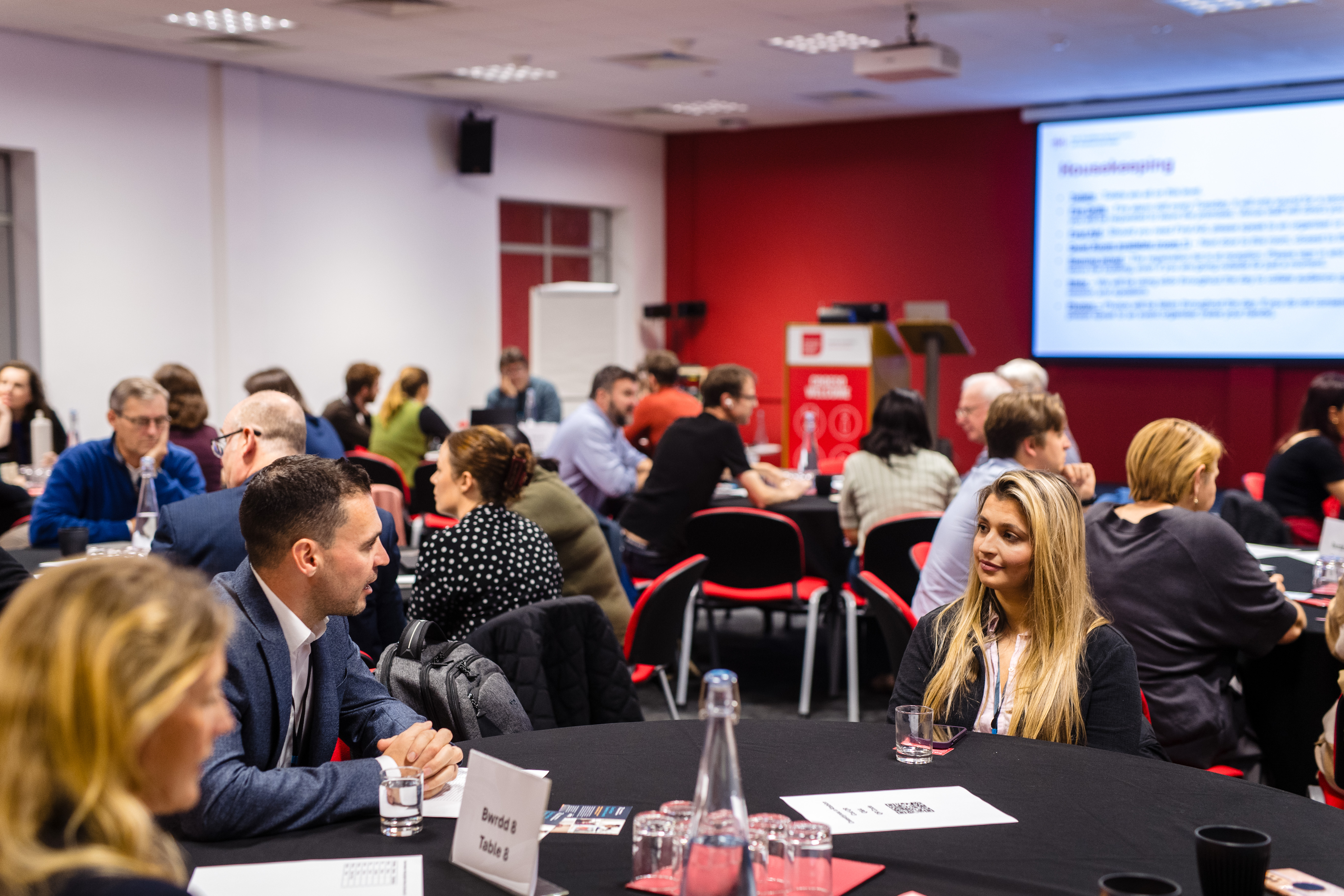 A photo from the latest AMS event. A large group of people are sitting around tables and talking.
