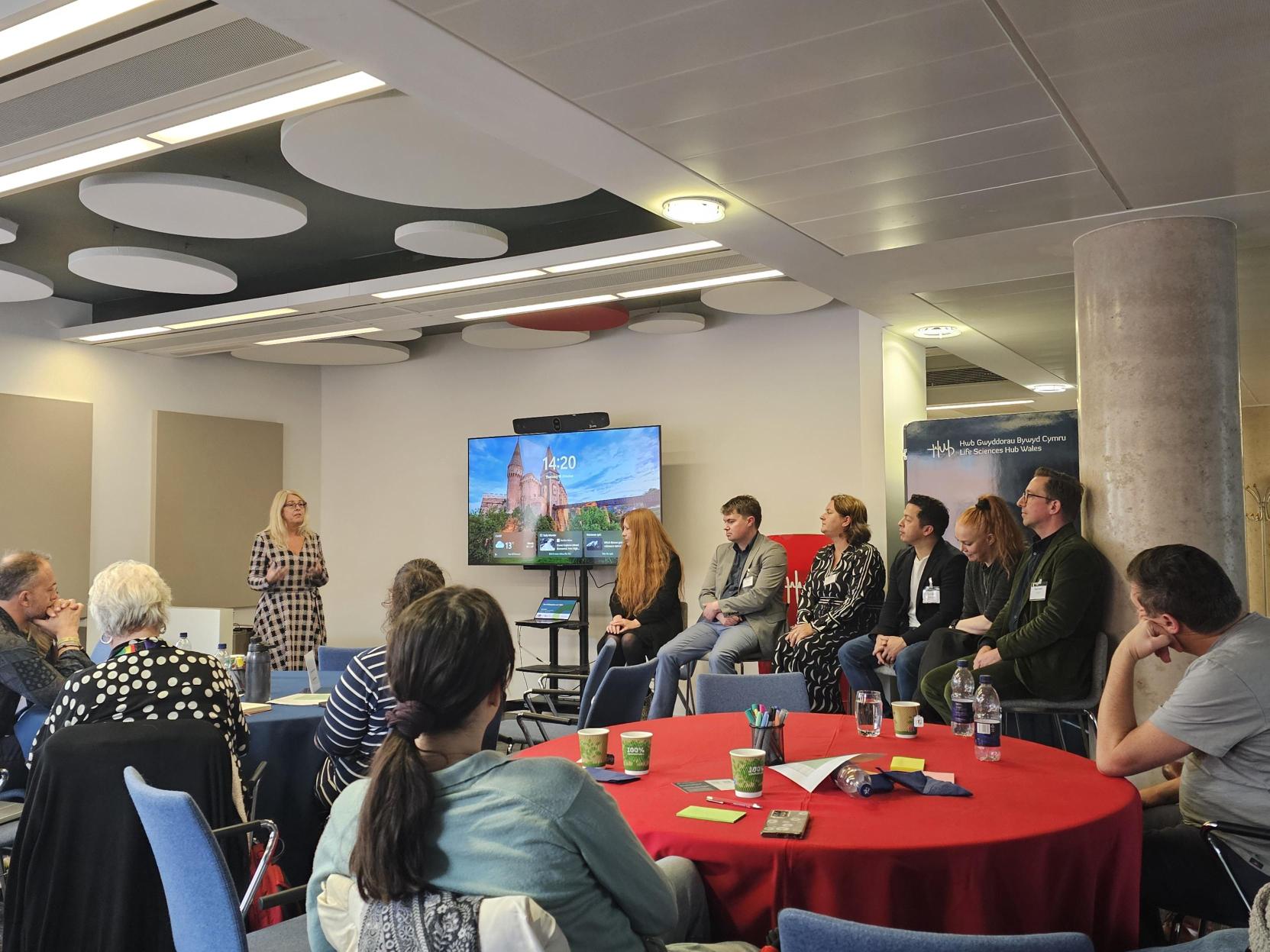 An image from the Mindset event. A group of people sitting around red tables, listening to a presentation.