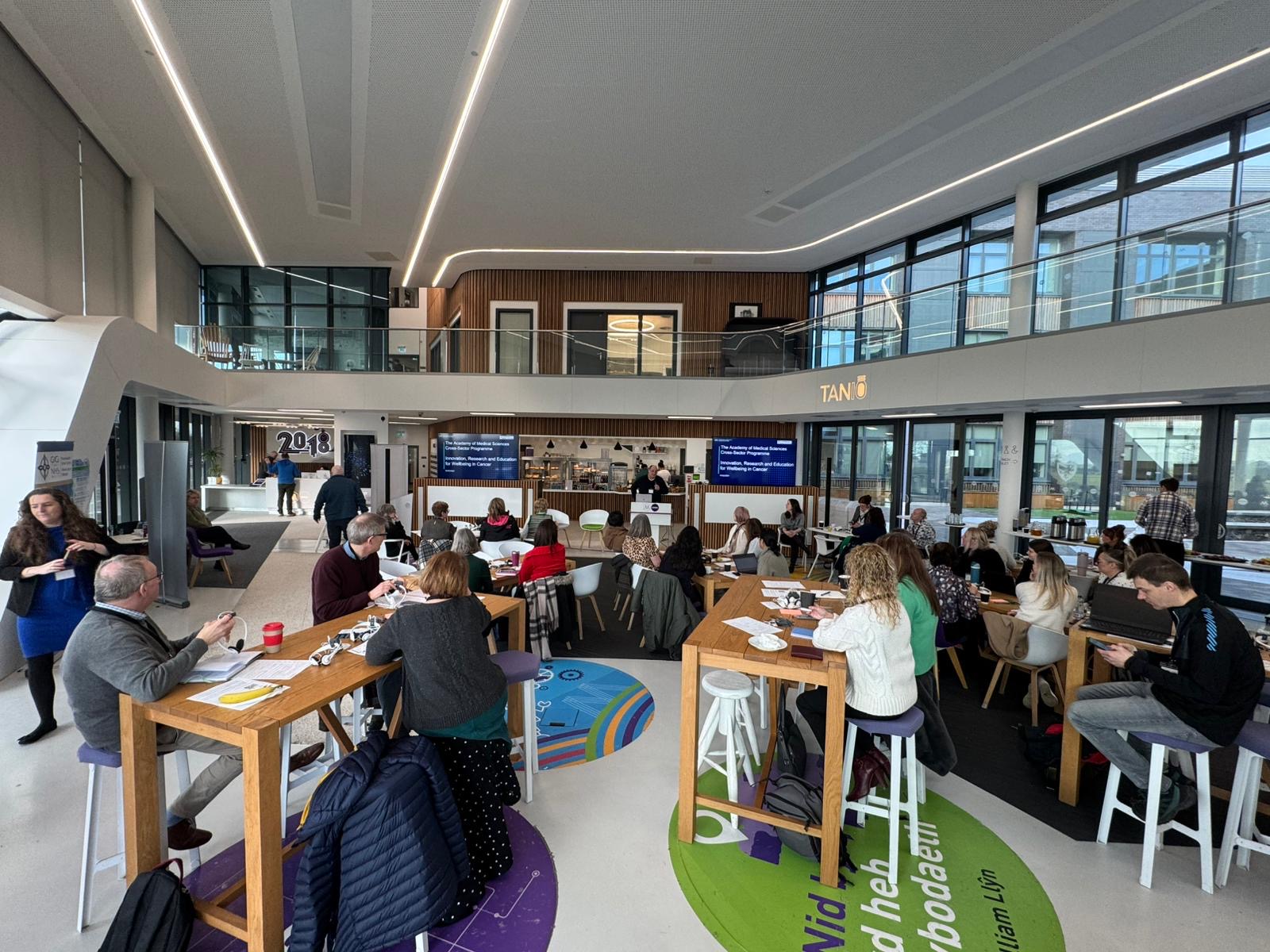 Room full of people at an event. Everyone is sitting at high tables. 