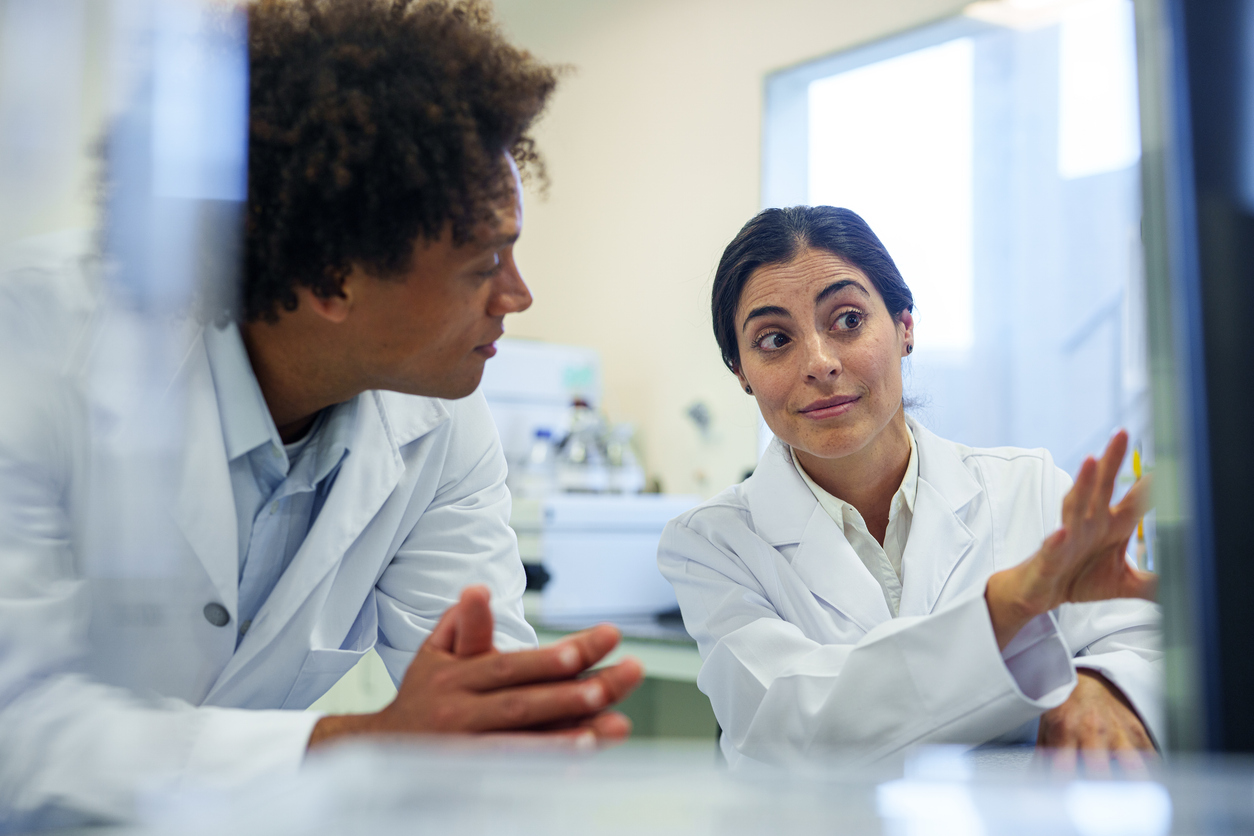 Woman and man sitting at a table in a lab, speaking. 