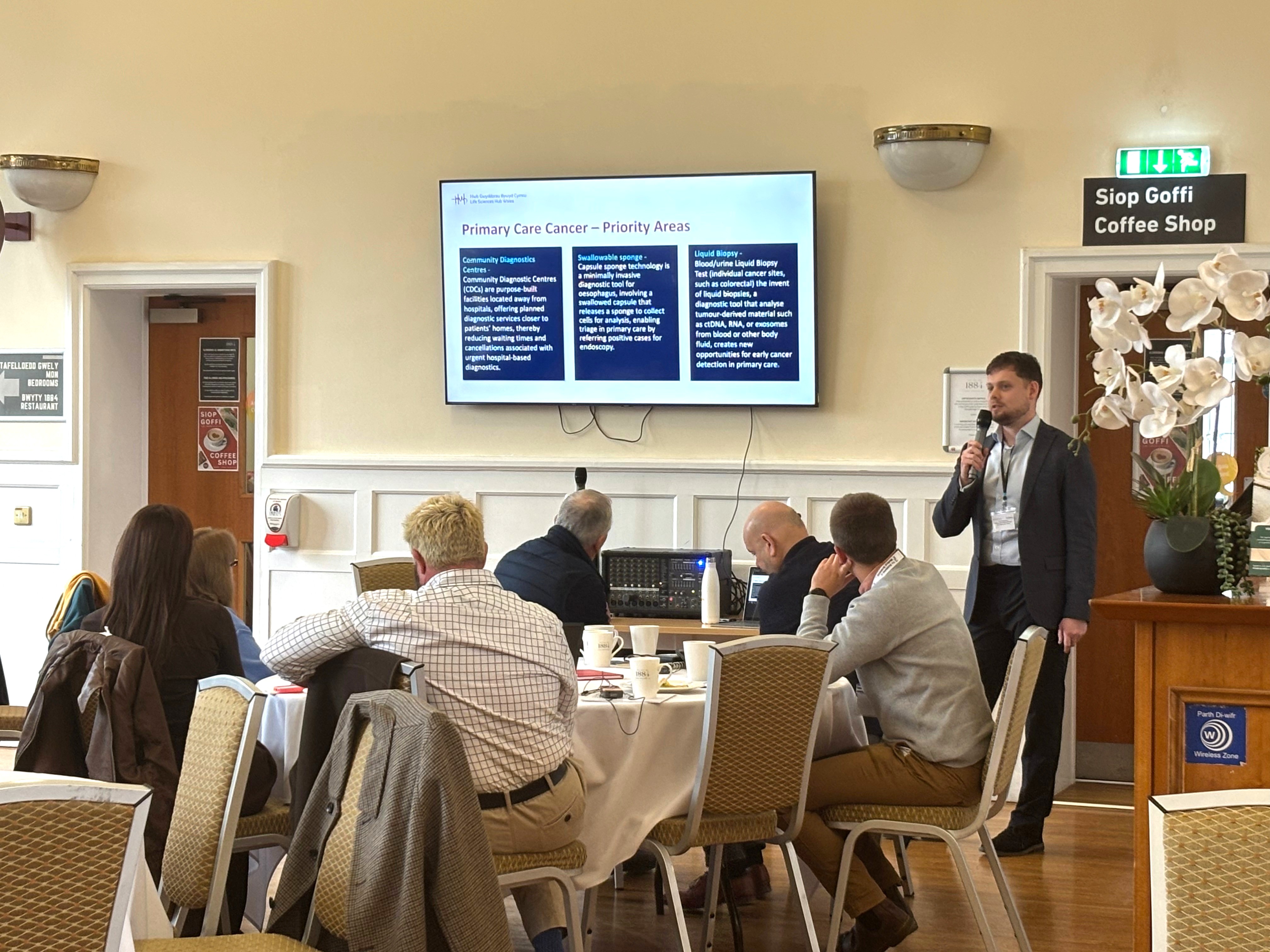 James Bourne presenting to a room full of people. People are sitting around tables.