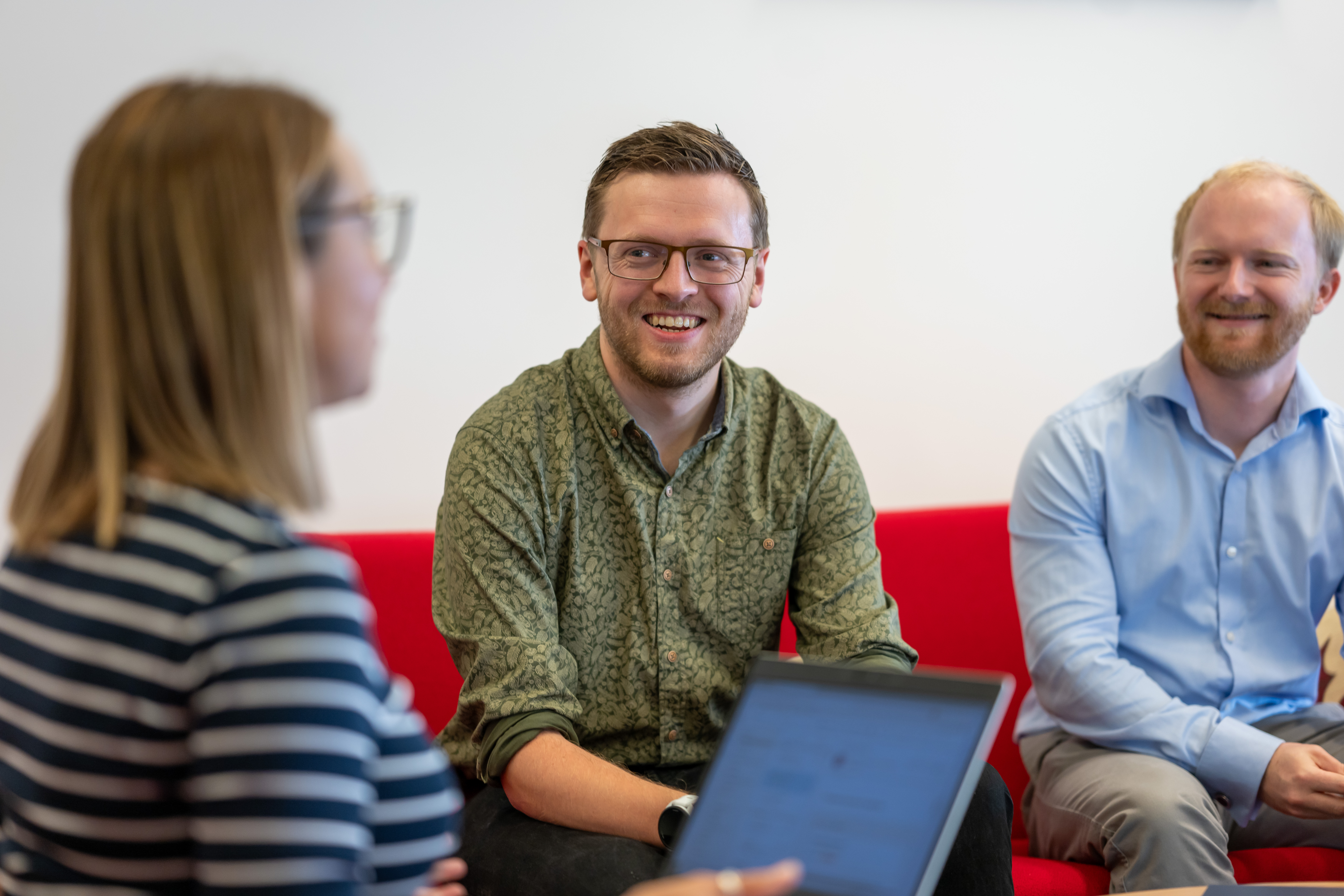 Three people laughing and chatting on an office sofa.