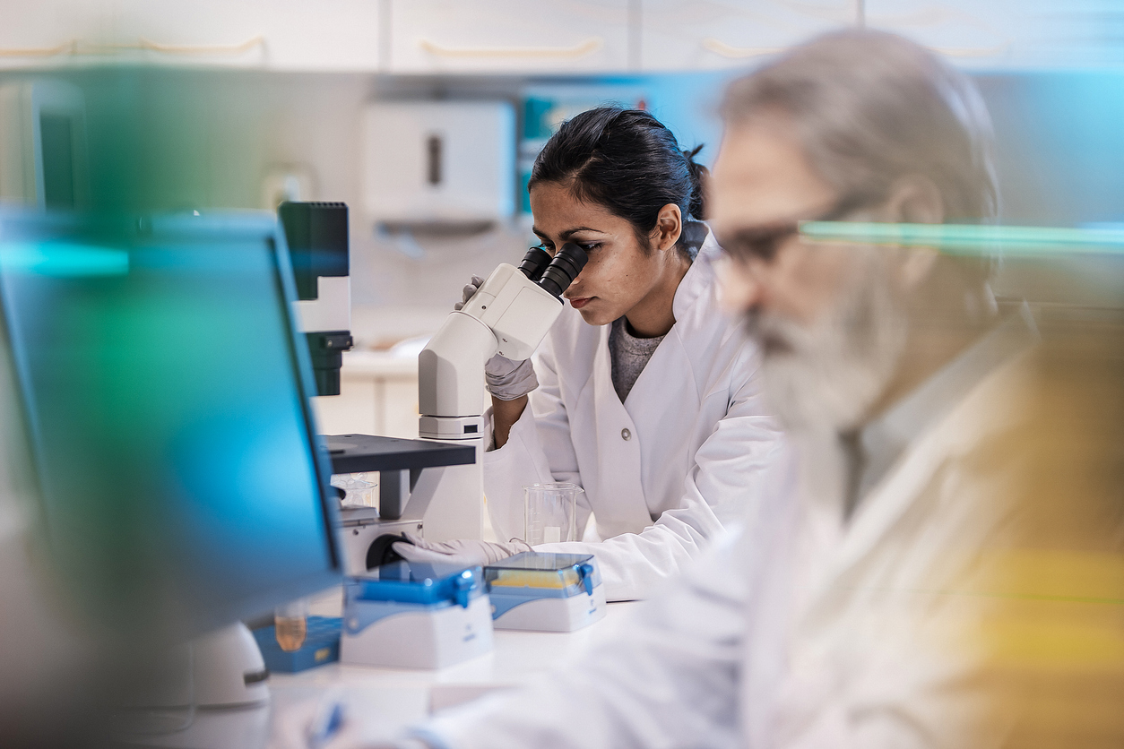 woman in a lab, looking through a microscope.