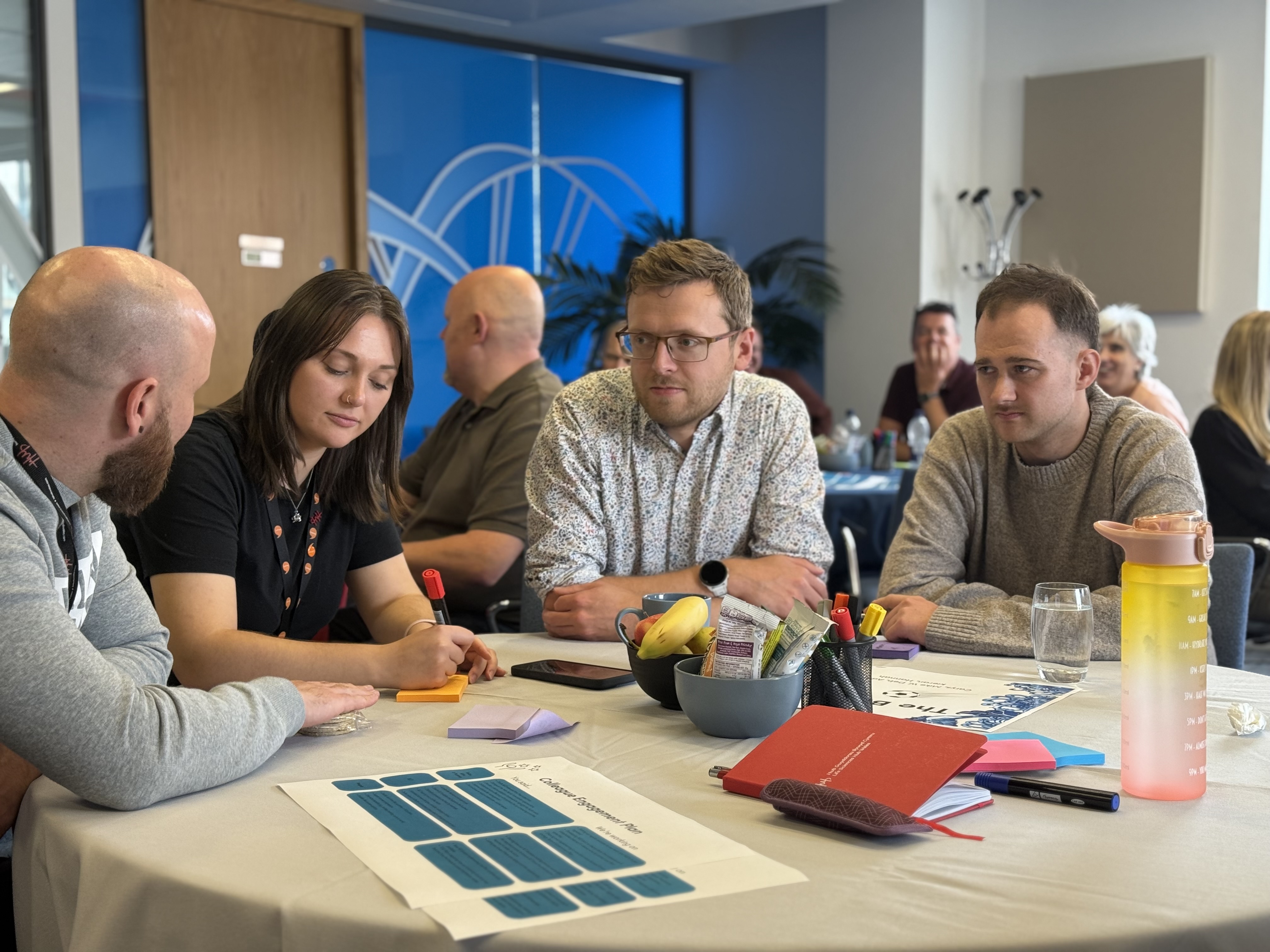 Four people sitting at table. Discussing and making notes.