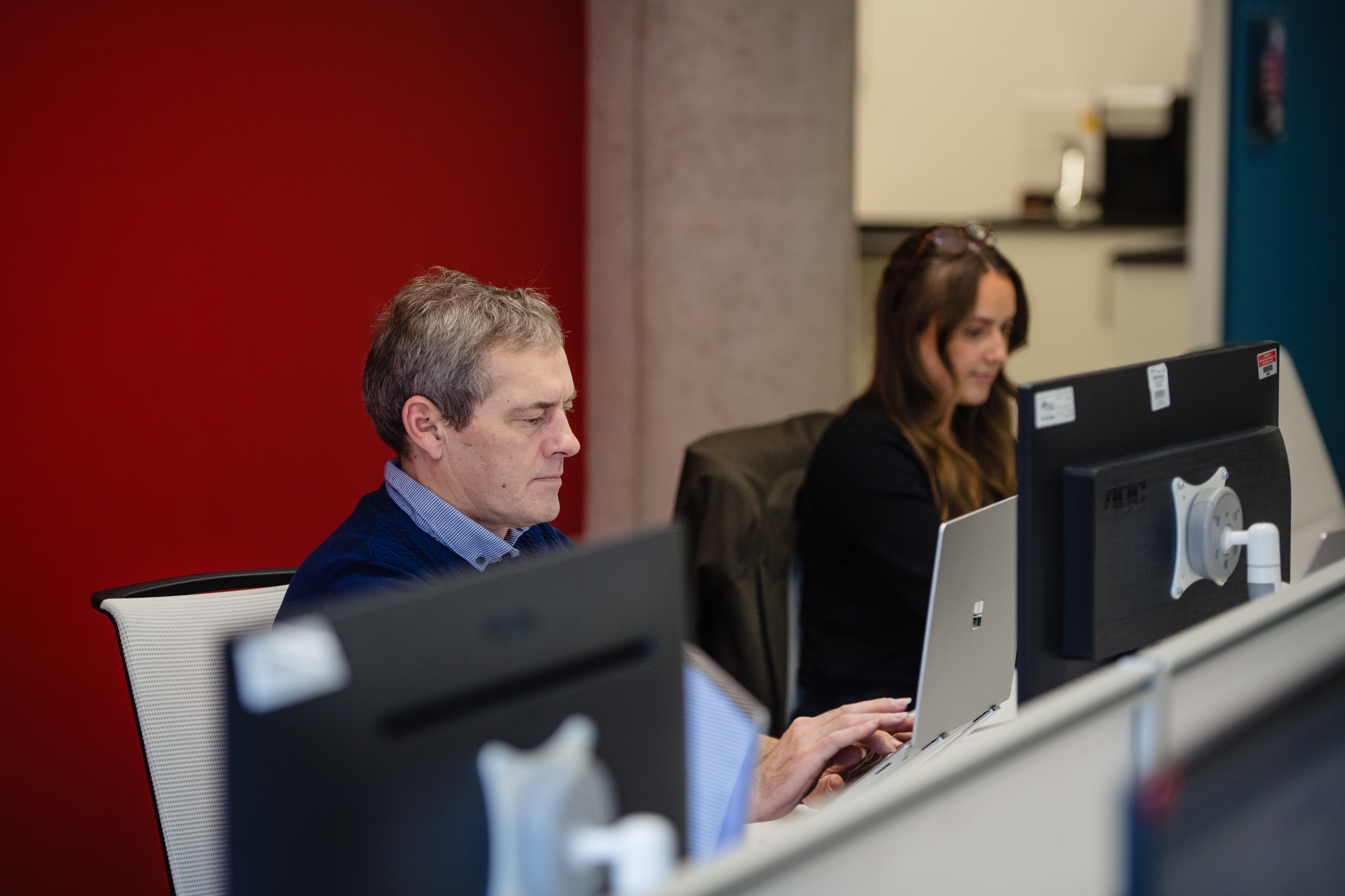 man and woman sitting side by side at their desk. they're both working on laptops.