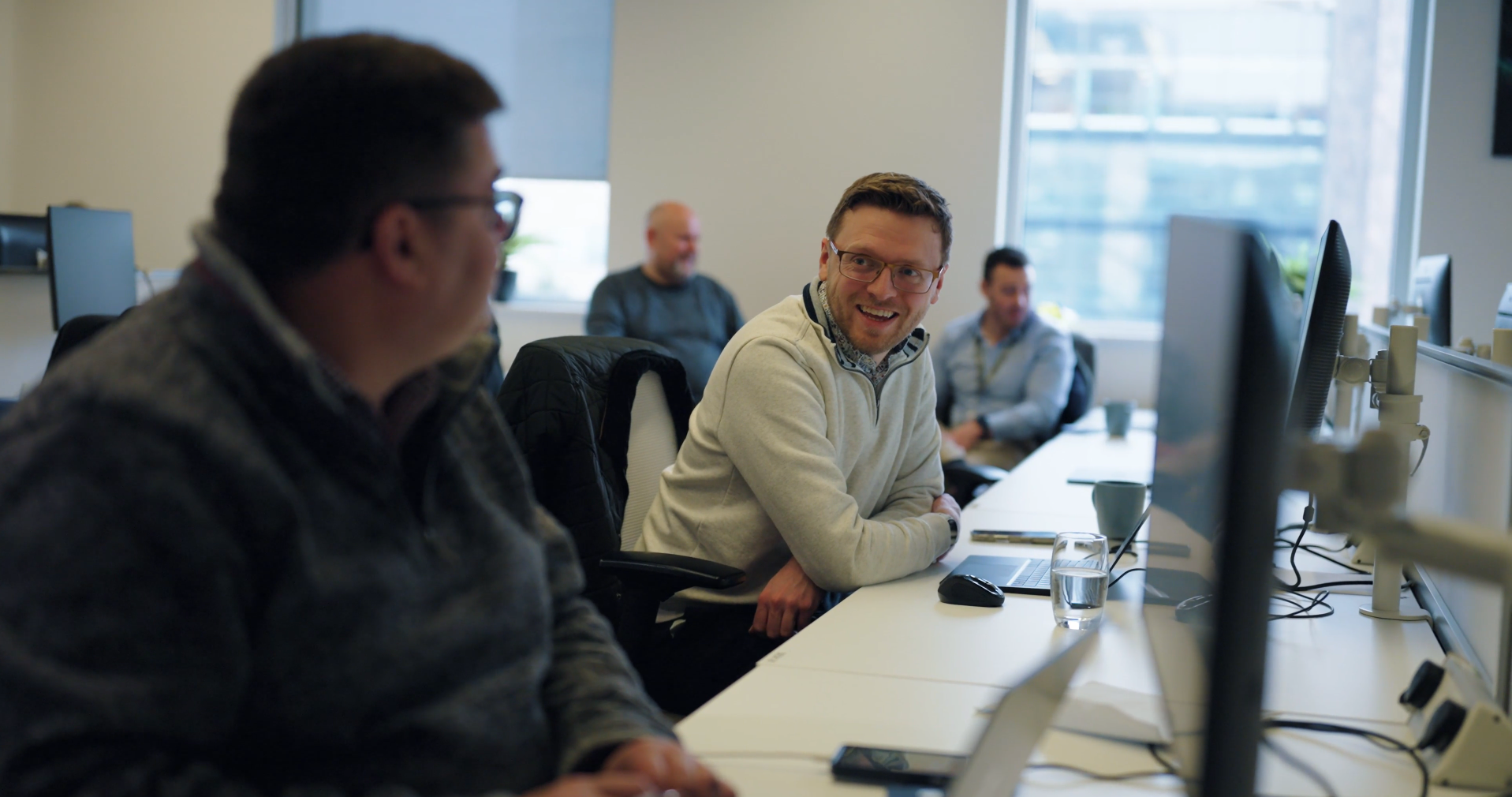 colleagues sitting at their desks, smiling and talking.