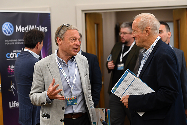 Two men speaking to each other. Both are in the middle of an exhibition hall. 
