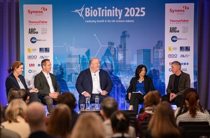 Five people sitting on stage at a conference. A crowd of people sit in front of them as they chat.