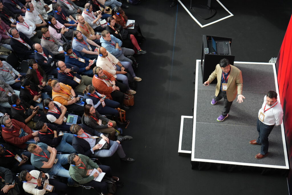 Birds-eye-view of crowd sitting whilst looking at presenters on stage.