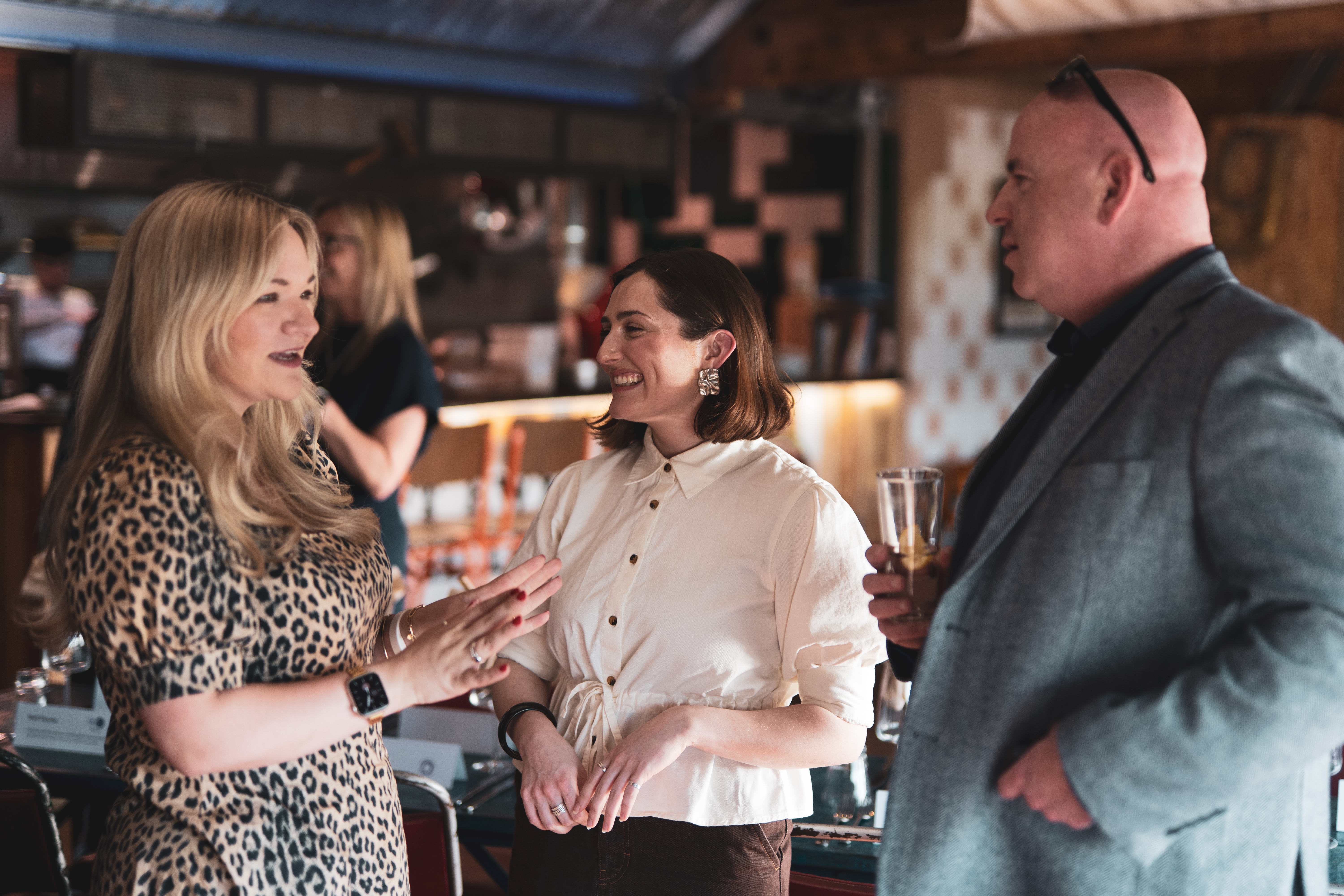 Two women and a man are standing at an event, talking.