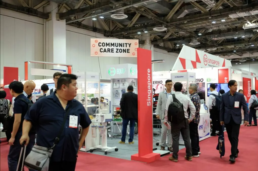 Conference exhibition area. There are stands all over with attendees talking.