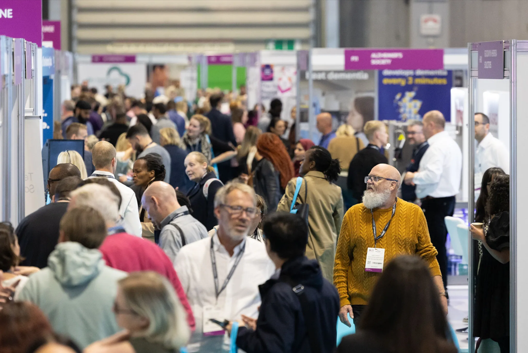 Crowd of people walking in between exhibition stands.