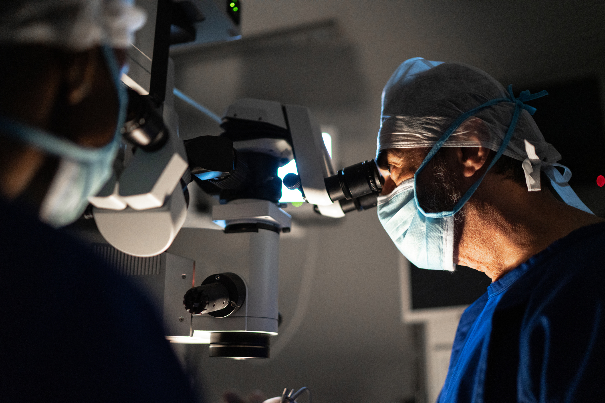 Surgeon dressed in PPE, looking through a lens whilst doing surgery,
