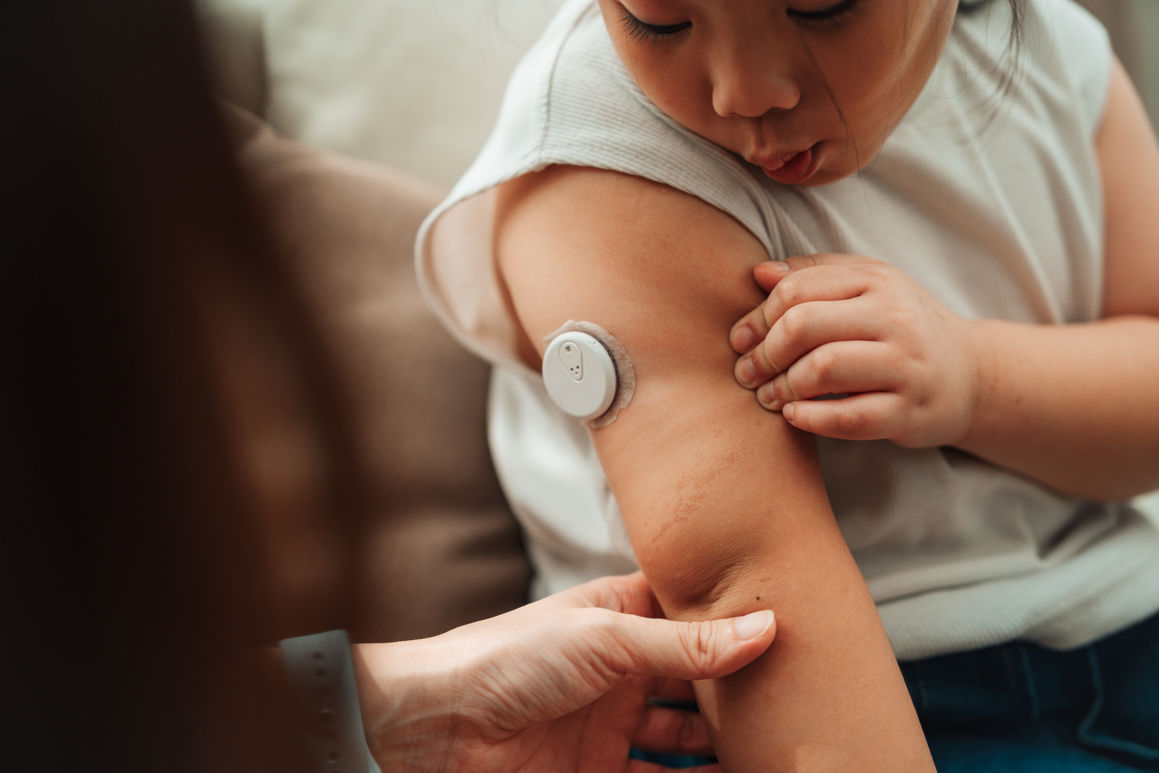 Mum using CGM device to check her daughter's blood sugar level, ensuring her health is closely monitored in real-time
