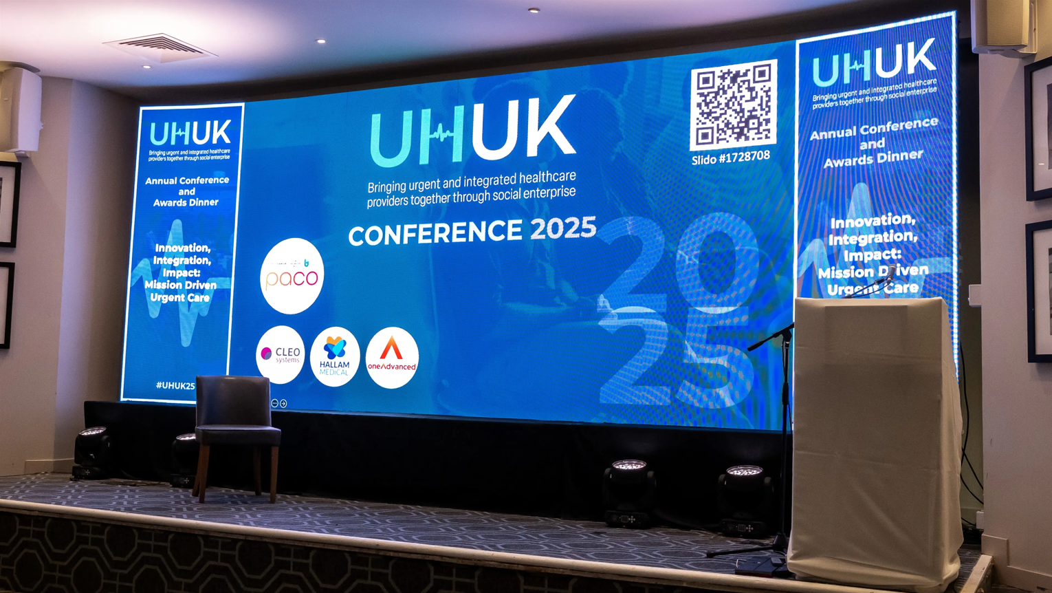 Conference stage with screens. Across the screens is a range of logos against a blue background.