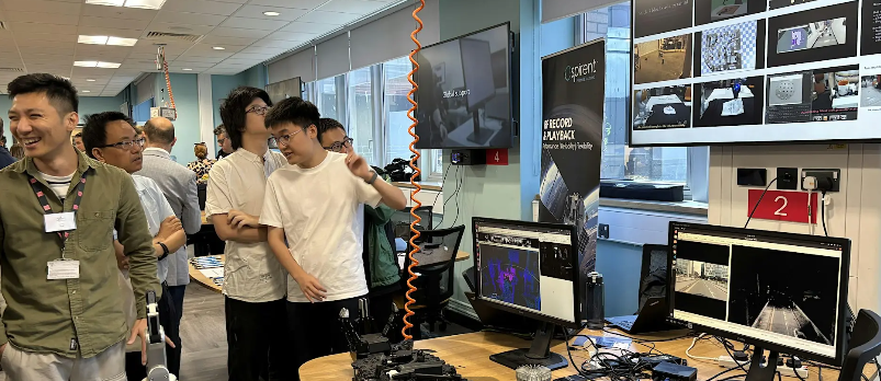 Group of people standing around a table with a display of computers on top.